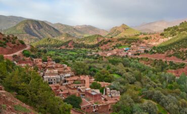 Breathtaking panoramic view of the Moroccan Atlas Mountains and a traditional Berber village nestled in a valley, representing an authentic cultural and natural escape for excursions from Marrakech, perfect for hiking and photography.