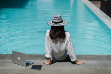 Digital nomad working remotely from a luxury all-inclusive resort in Morocco, near Marrakech, with a laptop by a sunlit pool, illustrating ideal telework and work-life balance.