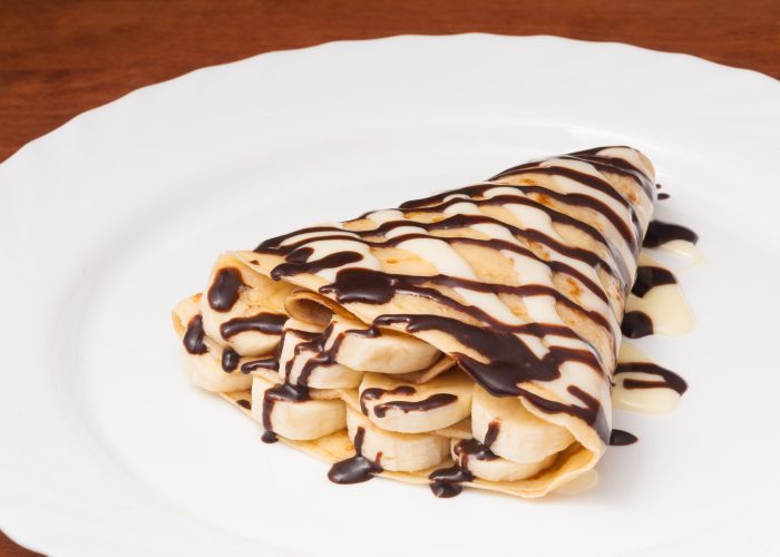 pancake with banana and chocolate on a white plate
